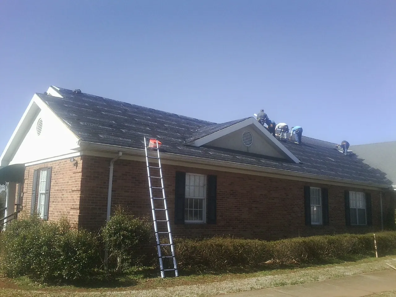 Crew tearing shingles off a brick ranch roof with a ladder set — Emergency Roof Repair work by our crew in Piermont