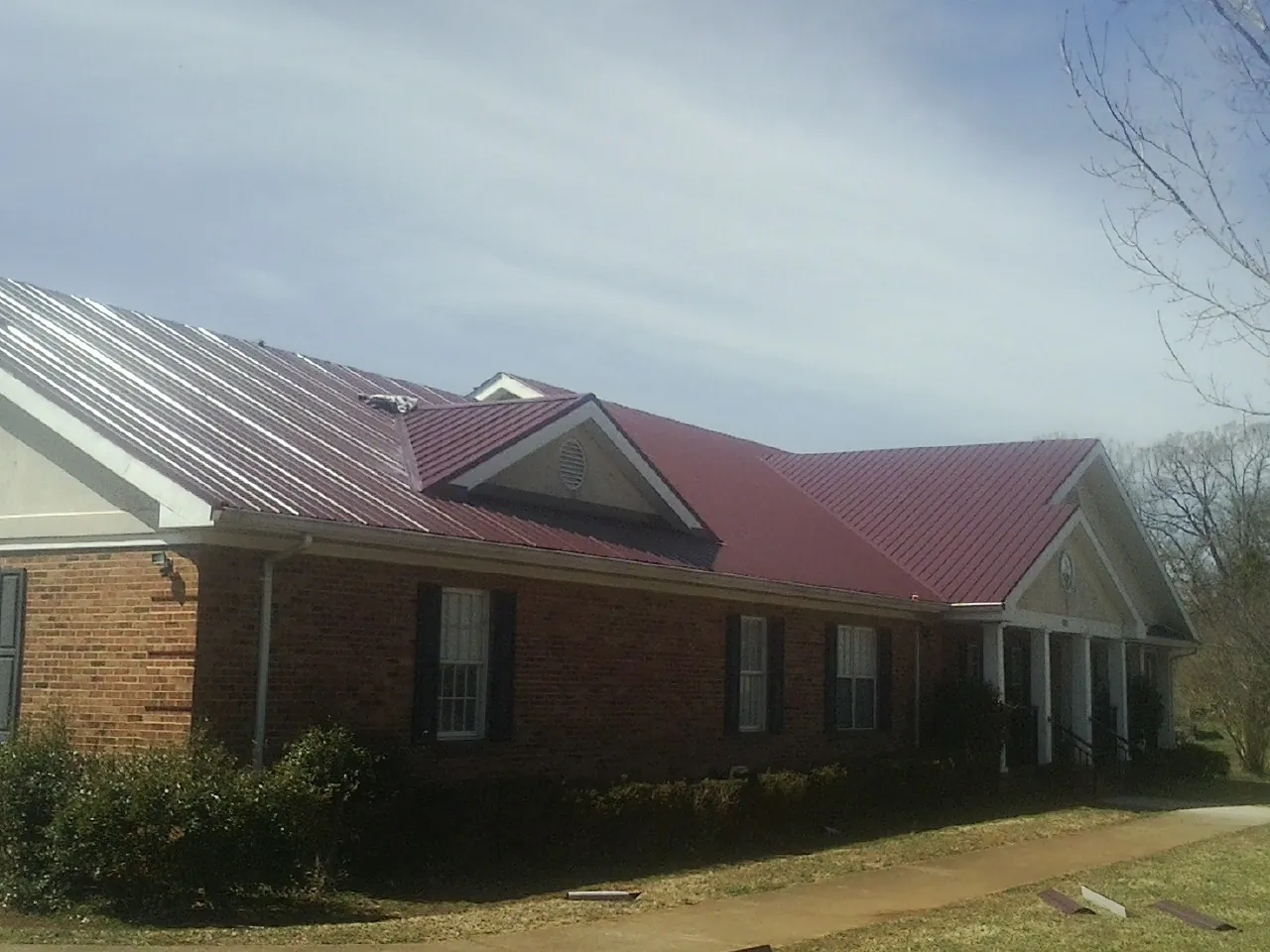 Red metal roof with gabled entries on a long brick building, from a Hail Damage Roof Repair job in Piermont