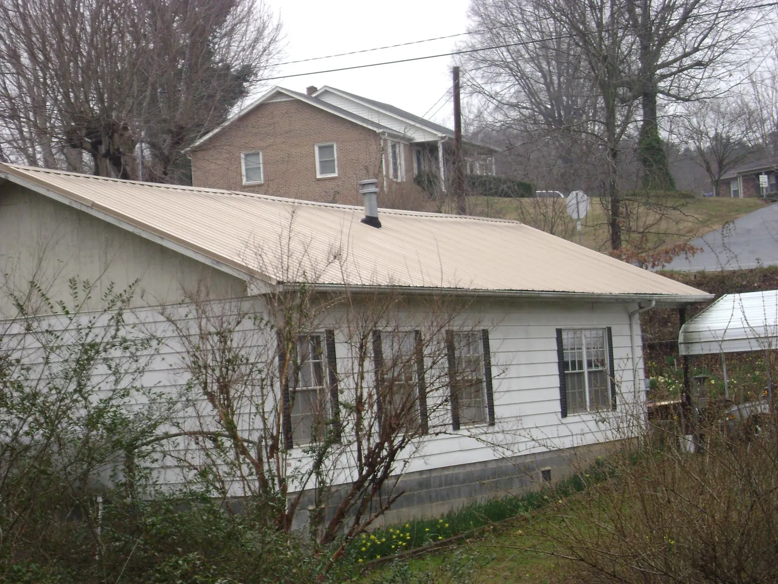 Tan metal roof on a white sided house set into a hillside — Commercial Roofing by Roofing Brothers in Piermont